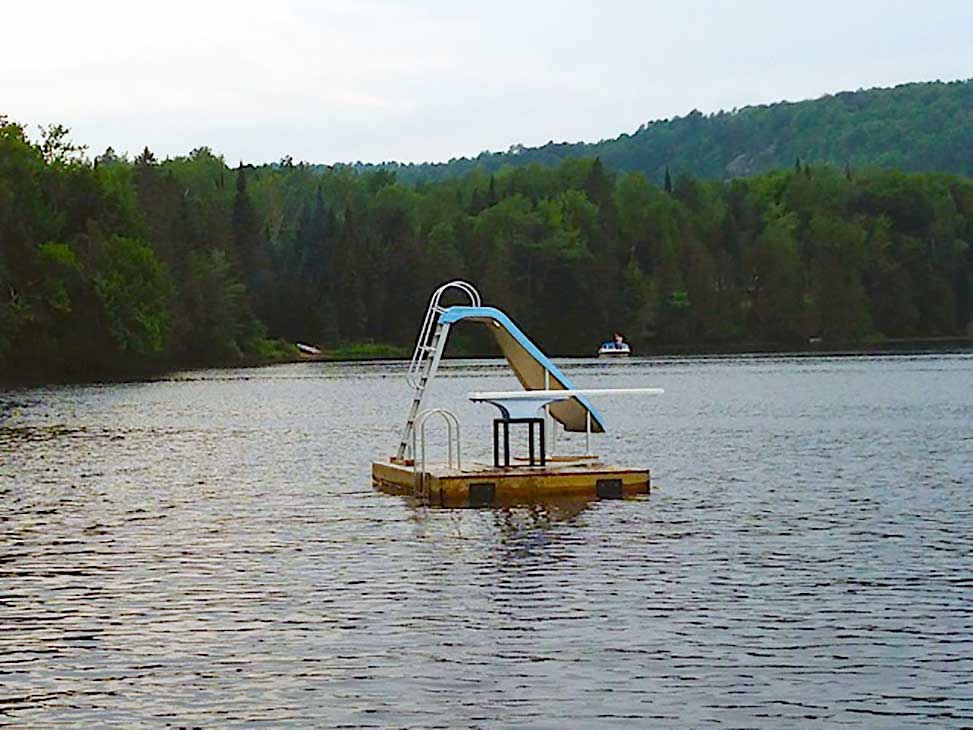 A floating raft with waterslide and diving board is shared by all cottages
